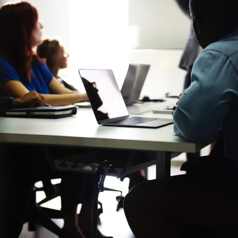 A group of adults using laptops at a table looking at an instructor off camera