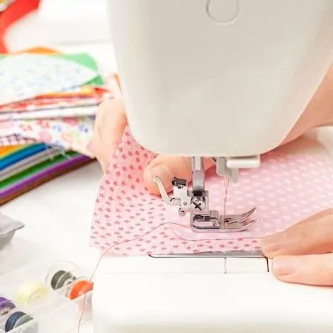 Hands guiding a fabric square through a sewing machine