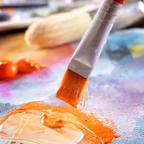 Bright orange acrylic paint being brushed onto a canvas.