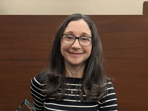 A photo of a woman with brown hair and glasses smiling warmly at the camera