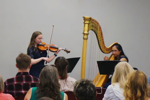 Two women playing a harp and violin to a crowd