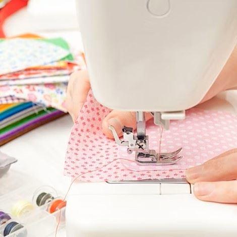 Hands guiding a fabric square through a sewing machine