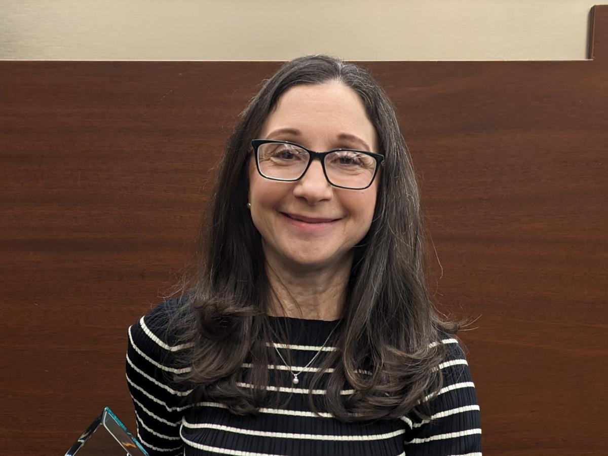 A photo of a woman with brown hair and glasses smiling warmly at the camera